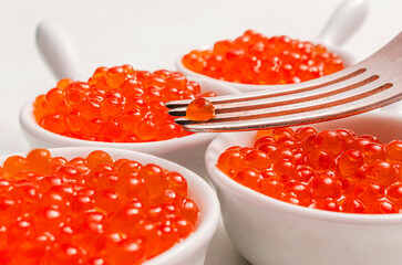 Red salmon caviar in white bowls with fork &mdash; luxury seafood delicacy macro close-up