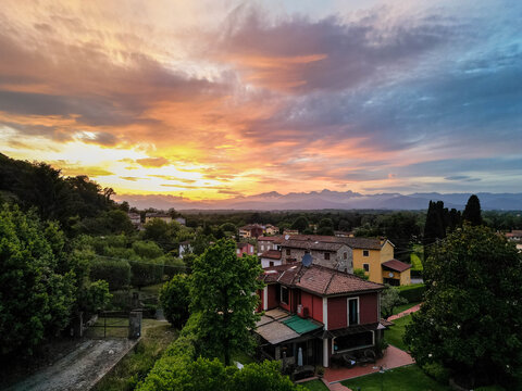 Aerial view of the Tuscan countryside during sunset, showing rustic village houses surrounded by olive groves, cypress trees, and rolling hills.