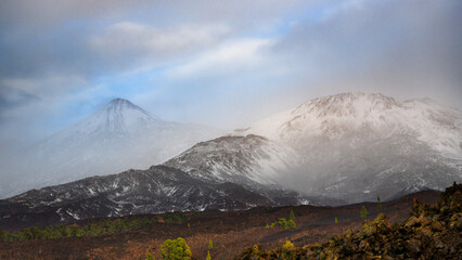 Fototapeta premium Snow-Covered Teide Volcano and Pico Viejo Under Misty Clouds, Tenerife, Canary Islands