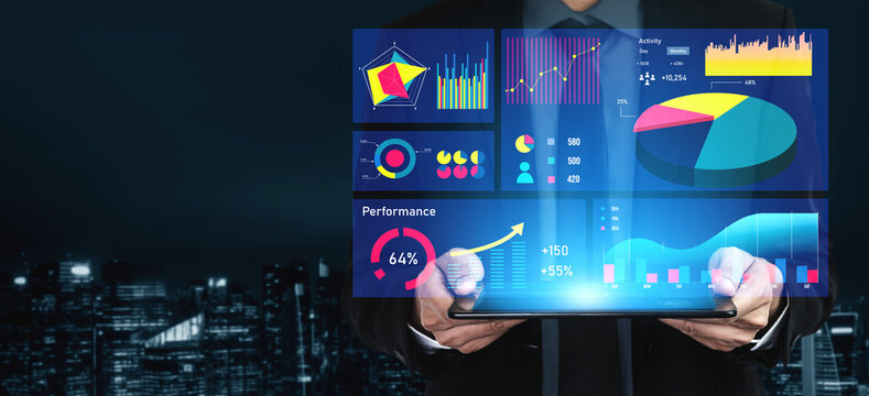 A businessman holds a laptop displaying digital performance metrics with colorful charts and graphs in a modern urban setting at night. Impute