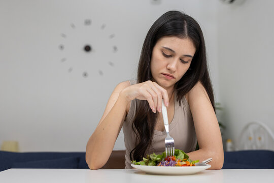 women looking bored or unhappy while eating salad at home. Concept for diet fatigue, food boredom, eating disorder awareness, lack of appetite or emotional eating habits.
