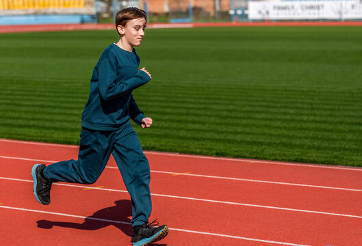 Children run. Young teen boy running on the running track at stadium outdoors. Kid exercising in athletics. Young athlete in race competition. Healthy outdoor sport for kids