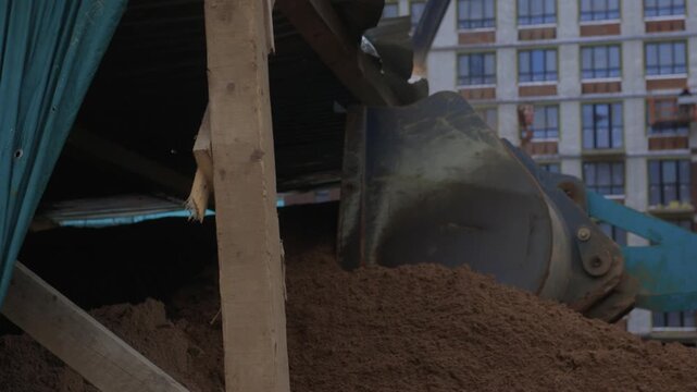 Industrial equipment transfers earth material at city construction site, Heavy machinery deposits soil into designated stockpile near highrise buildings under cloudy sky