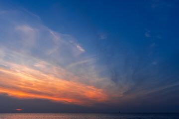 Fototapeta premium Sunset over the autumn sea, the bright colors of the red sun behind the clouds, tranquility after a stormy summer and a trip to the sea for relaxation
