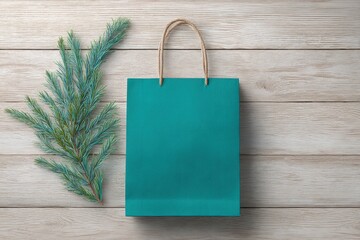 Teal paper shopping bag sits atop light wood planks, complemented by a sprig of evergreens.