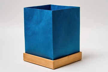 A simple, square, teal-colored box rests on a light wooden base against a plain background.