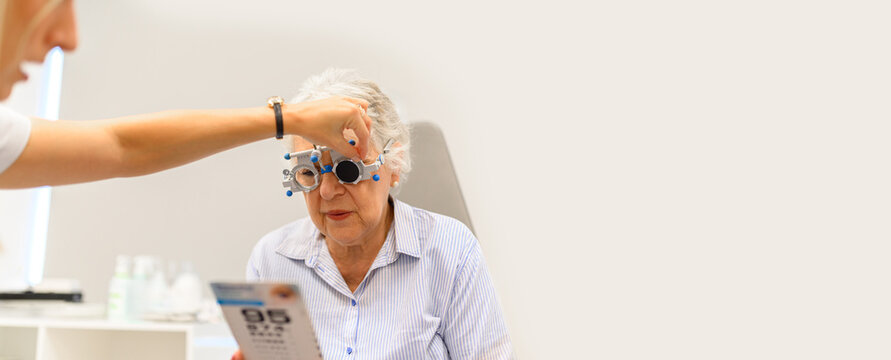 Female ophthalmologist adjusting phoropter lenses while senior woman reading eye chart during vision test at clinic