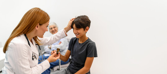 Senior woman looking at pediatrician giving prescribed pills to boy while comforting him by touching his hair in hospital