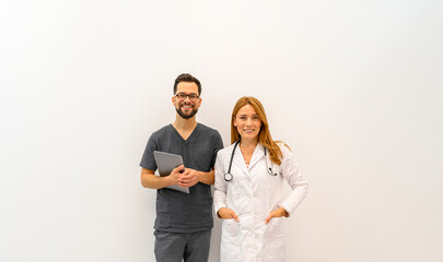 Portrait of confident male doctor holding laptop standing with female coworker against white background in clinic