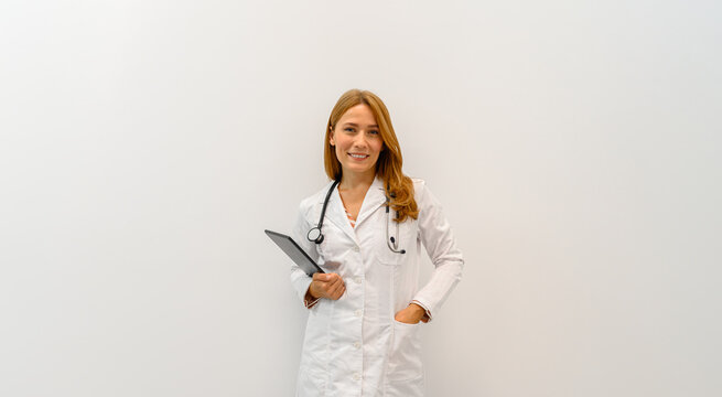 Portrait of smiling female ophthalmologist in lab coat with stethoscope and digital tablet standing on white background