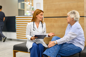 Obraz premium Female doctor holding clipboard explaining medical reports to senior patient seated in clinic hallway
