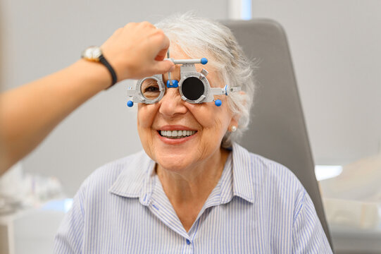 Hand of doctor adjusting phoropter lenses as senior woman undergoes vision test during eye examination at clinic