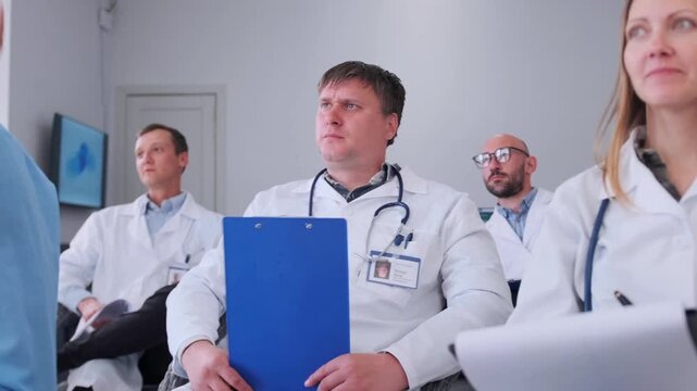 Medical professionals attentively listen to a lecture, making notes on clipboards and asking questions to clarify details during a clinical seminar.