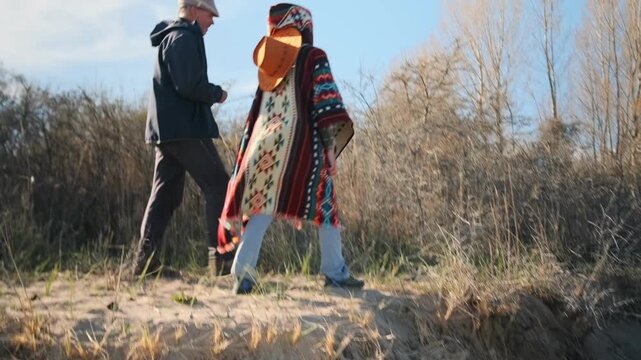 Adult man and young woman walking side by side in nature, talking and enjoying the moment. Ethnic patterned poncho, casual lifestyle, scenic travel and authentic outdoor atmosphere.