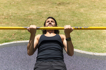 Close up of young latin man doing pull ups on a crossbar at a park