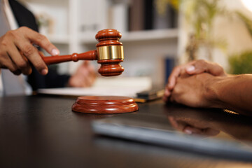 A man is holding a gavel and a pen while looking at a contract. The man is a lawyer and is discussing the contract with another person. Scene is serious and professional
