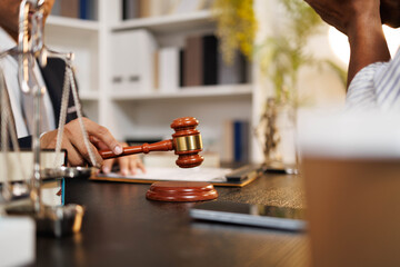 A man is holding a gavel and a pen while looking at a contract. The man is a lawyer and is discussing the contract with another person. Scene is serious and professional
