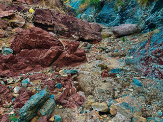 Gorge with aubergine-red and greyish-bluish rocks and some vegetation.