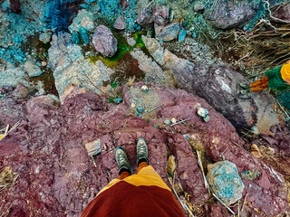 Male legs in brown shorts and grey boots and female legs in green shorts standing on purple rock in...