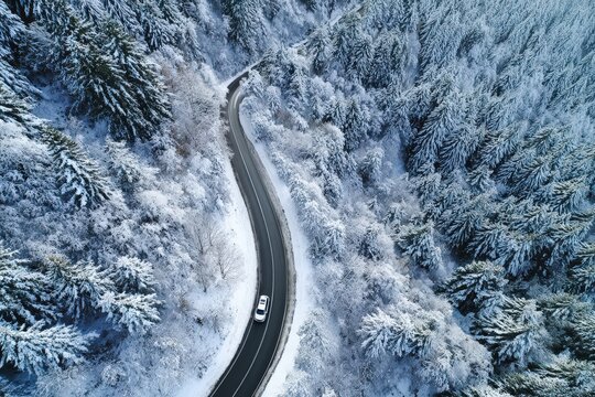 A winding road snakes through a snowy forest, showcasing a winter wonderland landscape.