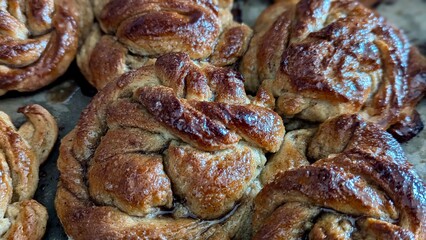 Freshly baked golden brown cinnamon buns with a glistening sugar glaze, cooling on a baking sheet.