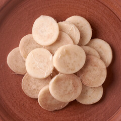 close-up of pale beige banana stem pith slices in a rustic terracotta bowl, fibrous vegetable texture in earthy clay dish, traditional food and asian cuisine preparation