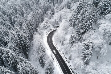 A winding road snakes through a snowy forest, a solitary white vehicle navigating the winter landscape.