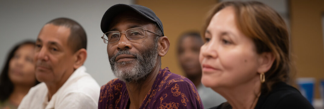 A diverse group of adults attentively listening during a discussion or presentation, highlighting the importance of communication and engagement in collaborative learning environments.