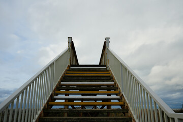 Weathered Outdoor Staircase With White Railings And Rusty Metal Leading Upwards To A Cloudy Sky In Towyn, North Wales, Uk