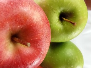 Vibrant close-up of fresh red and green apples with natural water droplets on their smooth skin. The crisp texture and bright colors highlight the freshness and juiciness of the fruit. A clean and app