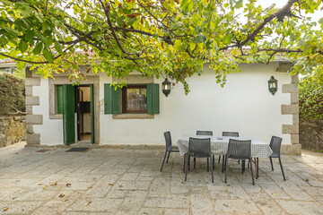 Natural fiber dining table on a terrace with an irregular stone facade and shade from Japanese arches in planters
