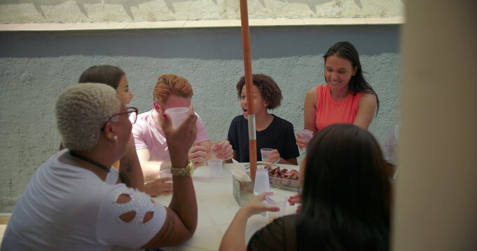 Diverse group of friends and family seated around table sharing laughs and enjoying food at outdoor backyard barbecue, celebrating joy and togetherness in summer - Powered by Adobe