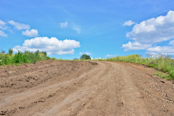empty and Winding Dirt Road with tire track Through Green Hills Under a Blue Sky