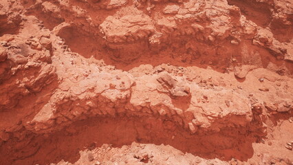 Rugged terrain showcases rich red hues and layered rock formations, inviting exploration of geological history. Sunlight casts dramatic shadows, enhancing the natural contours and textures.