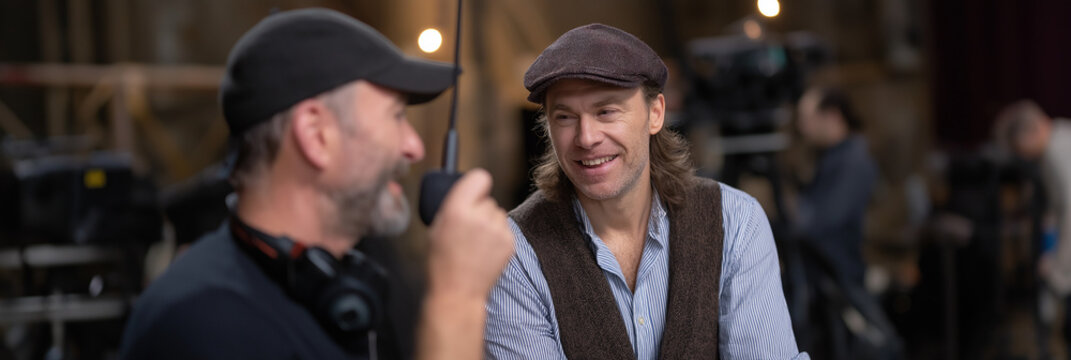Two filmmakers engaging in a conversation with a camera crew in the background, highlighting teamwork and creativity involved in the film production process.