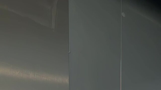 A person, dressed in whites, cleans a stainless steel wall, wiping it down with a damp cloth in a commercial kitchen setting during the early morning.