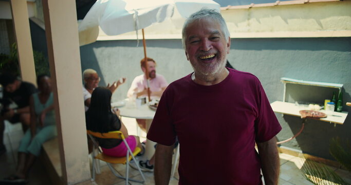 Elderly man laughing joyfully at a backyard barbecue, embodying happiness and connection amidst a lively gathering of family and friends