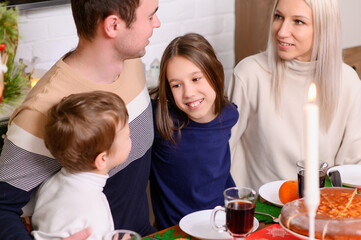 Family celebrates Christmas Eve by sitting around table for festive dinner with loved ones. Family enjoys traditional Thanksgiving feast by warm light of candles, surrounded by parents and children.