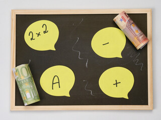 Small school blackboard with chalk and yellow blank sticky notes for personalization, counterfeit banknotes as a concept for school fees