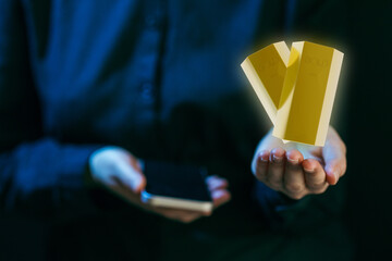 Hands hold smartphone and golden bars representing digital currency in a dark setting at night