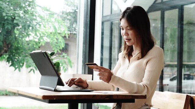 Young woman using a credit card to make online payments on her laptop in a modern cafe, representing digital lifestyle and e-commerce convenience.