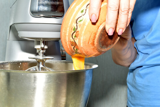 A woman adds beaten egg yolks to the metal bowl of a food processor.