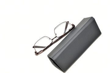 Dark colored glasses case and glasses with metal frames on white background.