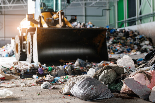 Industrial waste management facility with bulldozer handling garbage to conveyor of garbage recycling plant - Powered by Adobe