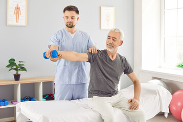 Man therapist helping an elderly patient with arm stretching and dumbbell exercise during a...