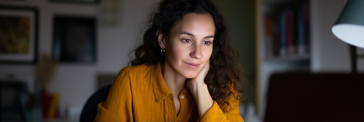 A thoughtful woman focuses on her laptop in a cozy room, reflecting diligence and aspiration in a creative workspace, capturing the essence of modern work-life balance.