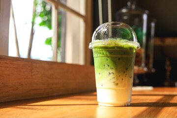 Iced green tea with milk in plastic cup on wooden table in a coffee shop.