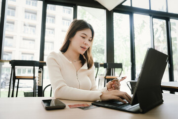 Obraz premium Young woman using a credit card to make online payments on her laptop in a modern cafe, representing digital lifestyle and e-commerce convenience.