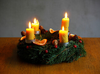 Close-up of a home made advent wreath with four burning candles made from beeswax and decorated with dried orange, red berries and nuts on wooden. Christmas catholic tradition. Christmas decoration.