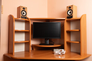 Modern workspace with monitor, speakers and headphones on a wooden corner desk near a pink wall.